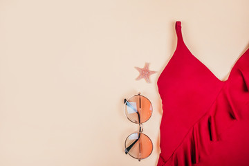 Summer fashion flatlay with gradient round sunglasses and red swimsuit with frills on the beige...