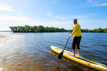 Adult man sails on a SUP board in large river and enjoying life