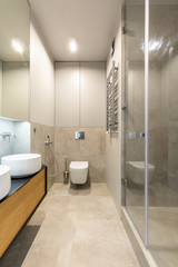 White washbasin on wooden cabinet in elegant beige bathroom interior with light. Real photo
