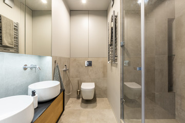 White toilet against beige wall in modern bathroom interior with washbasin. Real photo