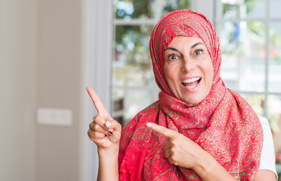 Middle aged muslim woman wearing hijab very happy pointing with hand and finger