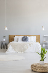 Plant on pouf in grey spacious bedroom interior with white chair next to bed. Real photo