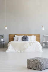 Patterned pouf in grey bedroom interior with blue pillow on wooden bed under lamps. Real photo