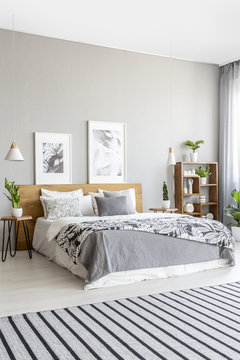 Striped carpet in grey bedroom interior with posters above bed with patterned blanket. Real photo