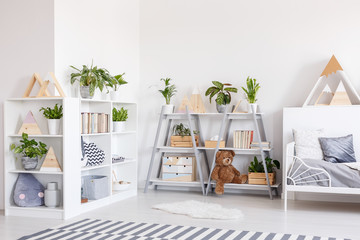 Plants on shelves in scandi grey bedroom interior with striped carpet near bed. Real photo