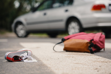Close-up of child's shoe and knapsack on a pedestrian lines after collision with a car - obrazy, fototapety, plakaty
