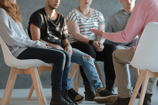 Group Of Young People Sitting In A Circle And Talking To Psychiatrist  During A Therapy