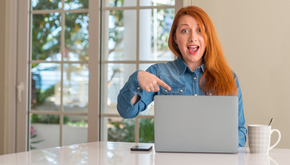 Redhead woman using computer laptop at home very happy pointing with hand and finger