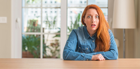 Redhead woman at home afraid and shocked with surprise expression, fear and excited face.