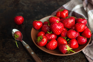 Fresh strawberry in a clay plate on concrete board wooden table.