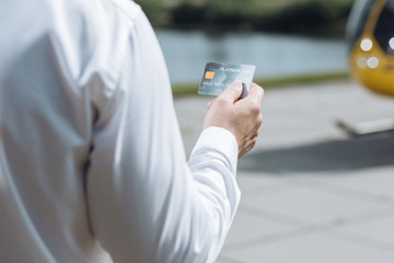 Convenient for payment. The focus being on a platinum card in the hand of a well-built young businessman standing in front of a helicopter