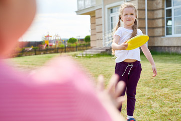 Portrait of cute  little girl throwing frisbee while playing with friend on green lawn in front...