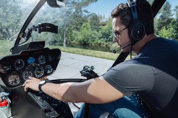 Precise parameters. Handsome young man sitting at a pilot booth of a helicopter and checking its...