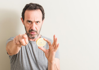 Senior man holding lemon fruit pointing with finger to the camera and to you, hand sign, positive...