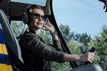 Fond of flying. The close up of a charming young woman sitting in the pilot booth of a helicopter and posing for the camera © zinkevych