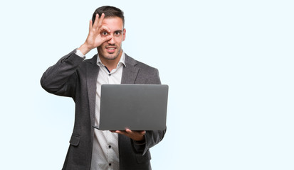Handsome young man using computer laptop with happy face smiling doing ok sign with hand on eye looking through fingers
