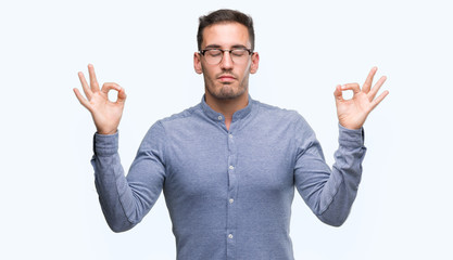 Handsome young elegant man wearing glasses relax and smiling with eyes closed doing meditation gesture with fingers. Yoga concept.