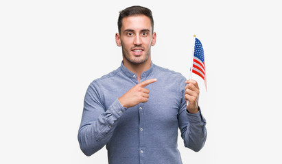 Handsome young man holding a flag of America very happy pointing with hand and finger
