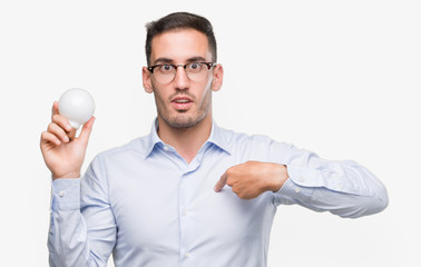Handsome young man holding lightbulb as idea with surprise face pointing finger to himself