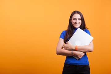 Cheerful beautiful young woman holding laptop over yellow background