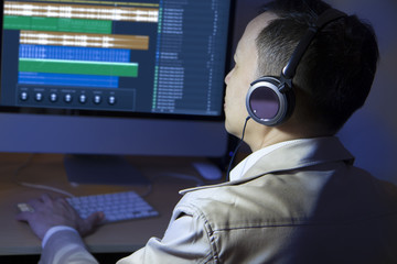 Asian male amateur sound editor edits and cuts sound audio on a computer, wears headphones monitor.