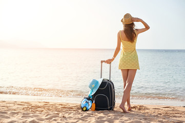 Beautiful young woman with a hat standing with suitcase on the wonderful sea background, concept of...