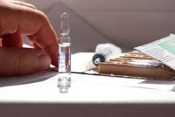 Novocaine in ampoule on the table and a doctor hand on the background.
