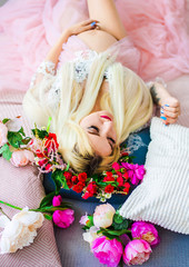 A pregnant blond woman in a pink dress with a wreath on her head lying on the bed