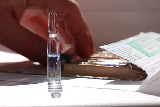 Novocaine in ampoule on the table and a doctor hand on the background.
