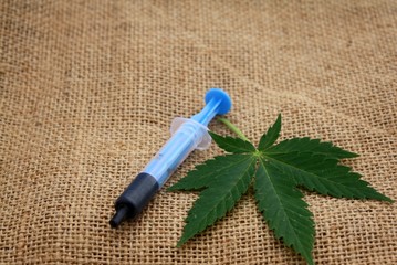 Hash oil phoenix tears medicine in little syringe with a cannabis marijuana leaf on linen jute...