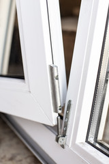 The movable part of the PVC window is connected to the frame using a metal hinge. Close-up.