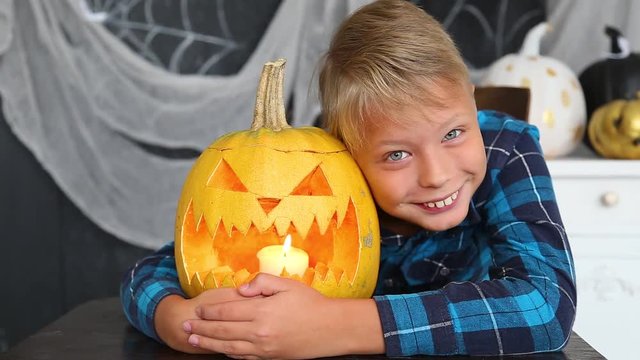 Closeup portrait of cute funny smiling kid with orange pumpkin at Halloween celebration. Boy posing for photo happily, looks at camera. Real time full hd video footage.