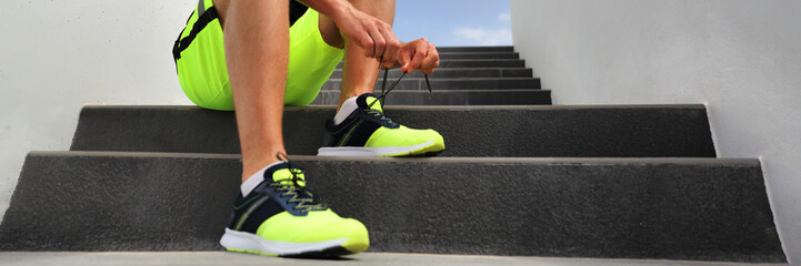 Runner man tying running shoes laces getting ready to run banner on city stairs. Healthy active lifestyle athlete jogging header panoramic crop.