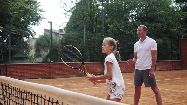 Coacher teaching young girl to playing tennis.