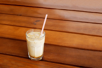 Iced coffee in a tall glass on wooden table. Copyspace.