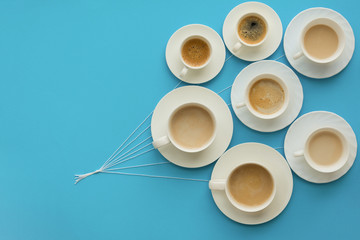 Hand holding coffee cups with milk and without in shape of balloons on blue paper background. Weather or good morning concept.