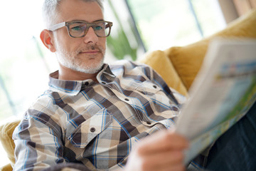Middle-aged man in kitchen reading newspaper