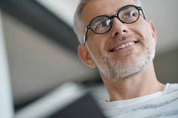 Trendy mature guy with eyeglasses reading book at home
