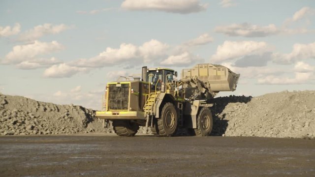 A full shot of a yellow truck dumping stones in slow motion. Camera zooms in    