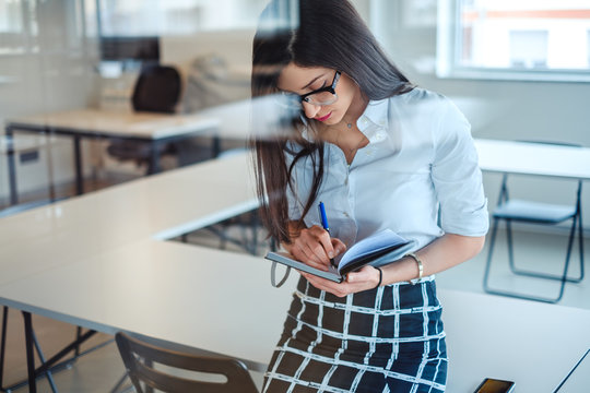 Sexy  businesswoman behind the glass writing in notebook