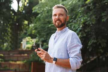 Happy young bearded man outdoors using mobile phone.