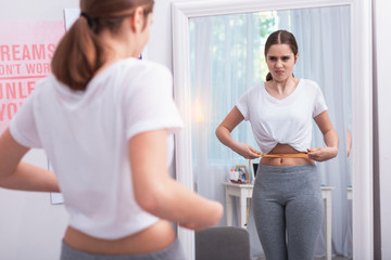 Downsize calories. Irritated teen girl using meter and gazing at mirror