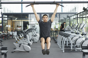 Fototapeta na wymiar Asian man working out in gym doing exercises with equipment in fitness center.