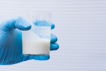 Checking, analysis of dairy products-kefir, yoghurt. A hand in a rubber glove holds a glass of...