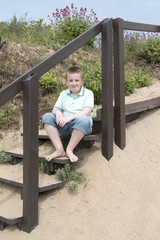 Obraz premium Portrait of eleven year old boy sitting on steps on a beach on a sunny day 