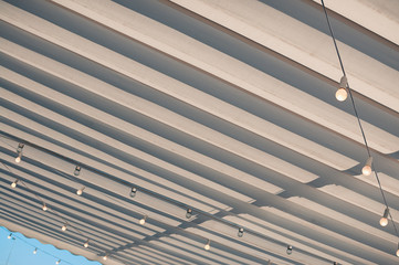 White roofing of a terrace in a street café or restaurant, with bulbs hanging under the awning, in...
