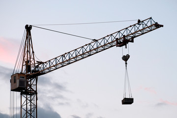 Construction tower crane with a load against the background of the evening sky.