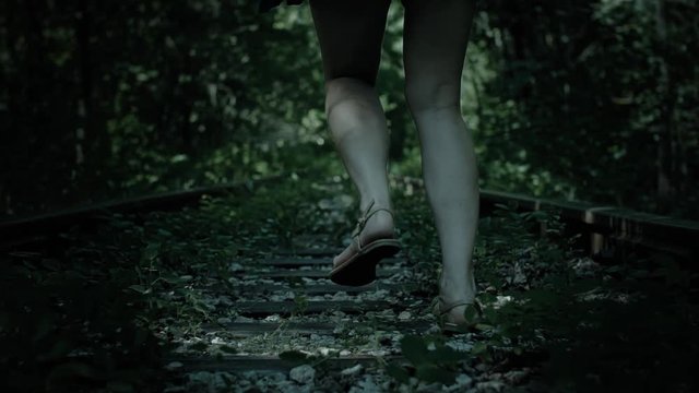 Night view of fleeing legs frightened girl. Railway in forest.
