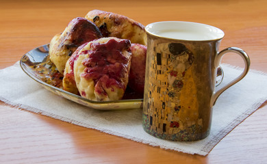 hot pie with berries, fried in oil, lined in a dish, a mug of cold milk with Klimt "the kiss", on a napkin