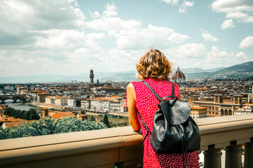 Woman tourist in red admires Florence Firenze (Duomo, Arno River, towers, cathedrals, tiled roofs of houses) from Piazzale Michelangelo, cityscape panorama top view, Florence, Tuscany, Italy